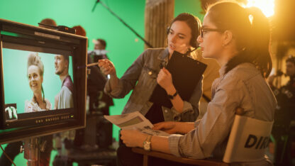 Talented female creator looks at display while talking with assistant on set of production
