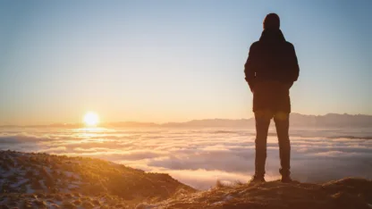 A man standing high in the mountains looking at the setting sun and the sunset horizon with a valley filled with clouds